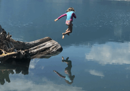 Charlotte, 7, leaps into a beautiful, still, isolated BC lake from a tree stump on a gorgeous summer day