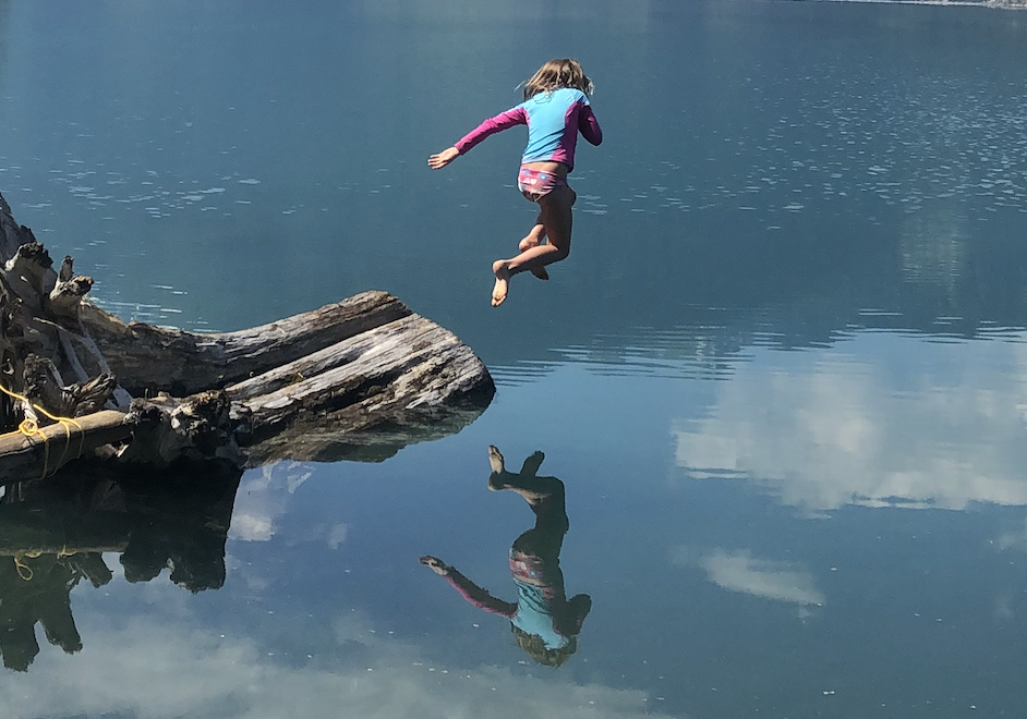 Charlotte, 7, leaps into a beautiful, still, isolated BC lake from a tree stump on a gorgeous summer day